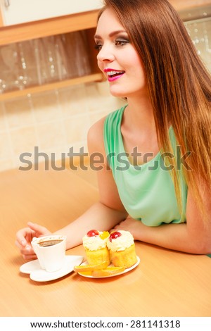 Woman with cup of coffee and delicious gourmet sweet cream cake cupcake and orange. Glutton girl sitting in kitchen with hot beverage having breakfast. Appetite and gluttony concept.