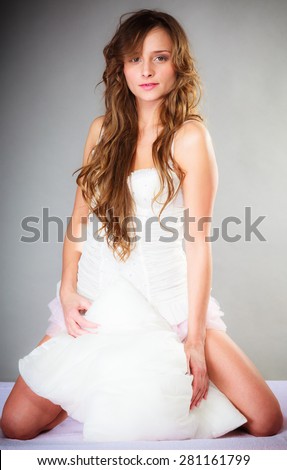 Sleep and wake up concept. Pretty young woman in curly long brown hair with pillow on gray background.