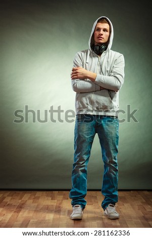Music leisure youth concept. Young hooded man teen boy in full length with headphones on neck grunge background