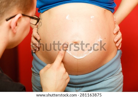 Pregnancy, parenthood and skin care concept. Family expecting new baby, having fun, man painting smiley face on belly of pregnant woman
