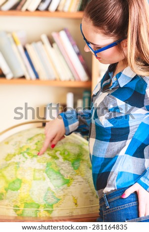 Education travel and geography concept. Young lovely woman female student in blue glasses in library pointing to globe