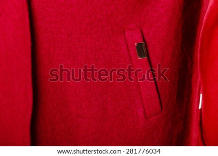 Closeup fragment of casual red coat with pocket and metal sign as background texture
