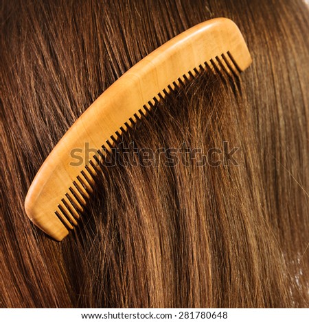 Hair care concept. Straight brown hair background with wooden comb