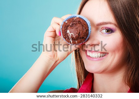 Diet sweet food and people concept. Funny woman holds cake in hand having fun covering her eye with cupcake blue background