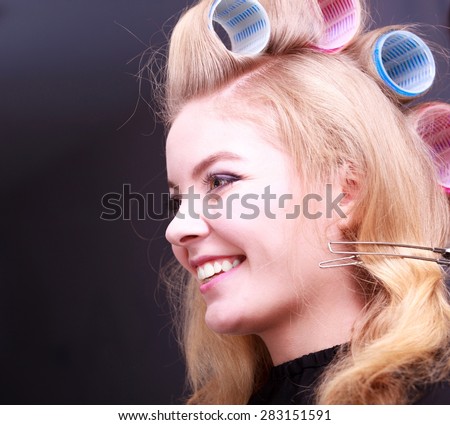 Beautiful young woman in beauty salon. Happy blond girl with hair curlers rollers by hairdresser. Hairstyle.