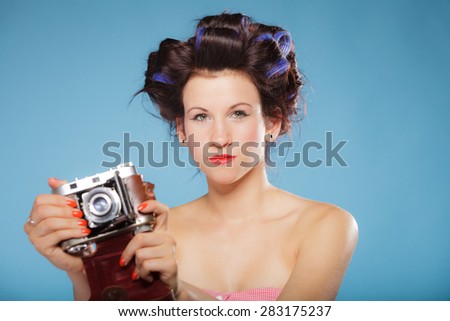 Pretty girl in hair curlers taking picture using vintage camera blue background
