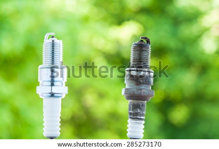 Auto service. Two car spark plugs new and old as spare part of auto transportation on blurry green background.