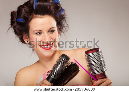Young woman preparing for date having fun, cute girl with curlers styling hair with many accessories comb brush hairdreyer on  gray