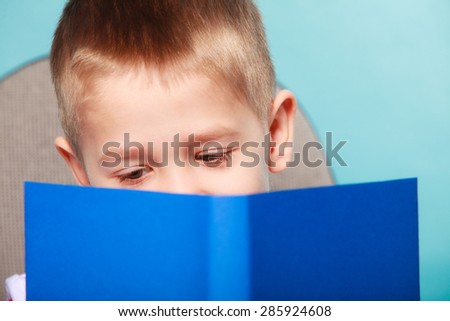 Education and school concept. Little boy reading a book, child kid on blue background holding an open book