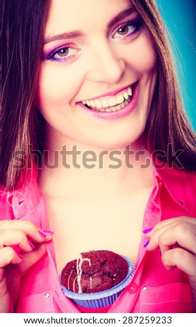 sweet food or sex for brighten moods. Smiling woman having fun holds chocolate muffin cake on her chest blue background