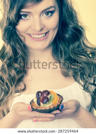 Bakery, sweet food and people concept. smiling cute woman curly hair holding fruit cake cupcake in hand yellow background