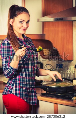 Woman in kitchen cooking stir fry frozen vegetables and tasting. Girl frying making delicious risotto. Dinner food meal.