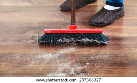 Cleanup housework concept. Closeup broom and female foots. Cleaning woman sweeping wooden floor.