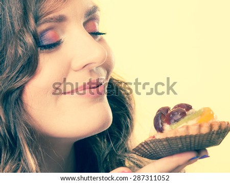 Bakery sweet food indulging and people concept. Cute attractive woman closed eyes holds cake cupcake in hand smelling yellow background