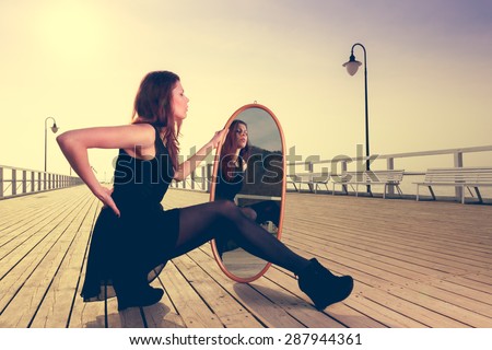 Solitude loneliness concept. Thoughtful young woman looks at the reflection in the mirror outdoors at sunset