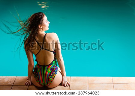 Relax, rest and recreation. Long haired woman back in colorful swimsuit on pool edge.