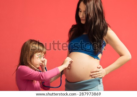 Pregnant woman with her daughter. Little girl excited about her coming sibling - listening to mother\'s tummy