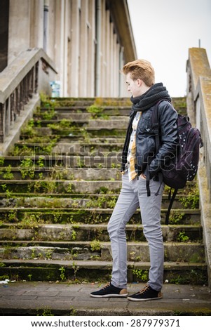 Fashionable handsome man in full length model posing outdoors on staircase in autumal cold day. Street fashion