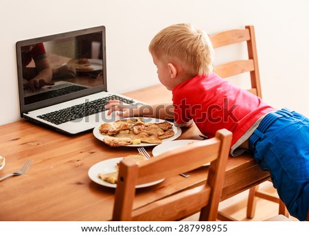 Children, technology and home concept  - little boy child eating meal while using laptop pc computer at home. Bad habits