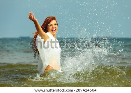 Vacation. Girl splashing water on the coast. Young woman having fun relaxing on the sea. Summertime.