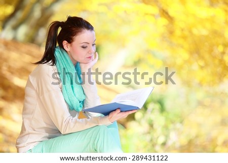 Fall lifestyle concept. Casual young woman girl relaxing in autumnal park reading book. Golden colorful leaves background