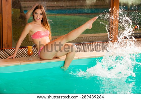 Relax, rest and recreation. Tropical drink and attractive splashing woman in pink bikini on pool edge.