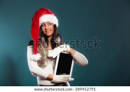 Technology internet and christmas time concept. Mixed race girl in santa claus helper hat holding computer, showing blank copy space on screen tablet touchpad on blue