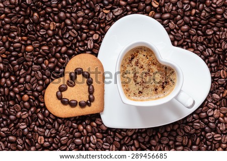 Coffee time concept. Heart shaped cup with cappuccino mocha and cookie gingerbread on coffee beans background. Top view