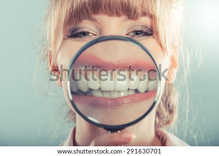 Happy young woman showing white teeth through magnifying glass.