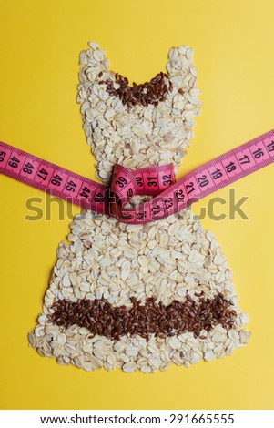 Dieting healthy eating slim down concept. Female dress shape made from oatmeal flax seeds with measuring tape around thin waist on yellow