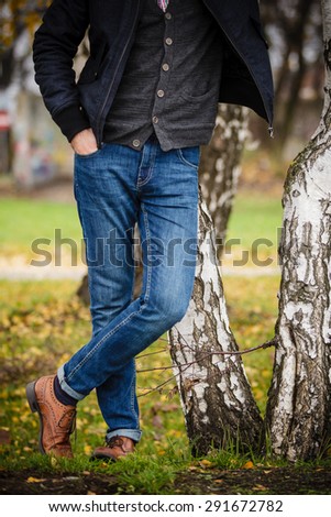 Fall season and people concept. Part of body stylish fashionable man in jeans posing against autumn birch trees.