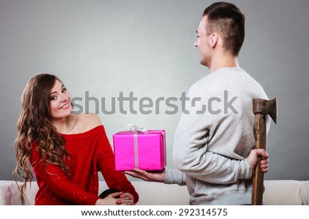 Sneaky insincere man holding axe giving gift present box to woman. Husband concealing hiding his true feelings from happy trusting wife. Untrue False intention. Relationship problems.