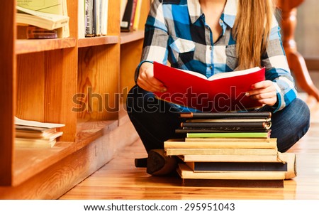 Education school concept. Clever female student girl sitting on floor in college library with stack books reading. Indoor