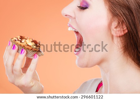 Bakery, sweet food and people concept. Woman face profile wide open mouth holds cake cupcake in hand orange background