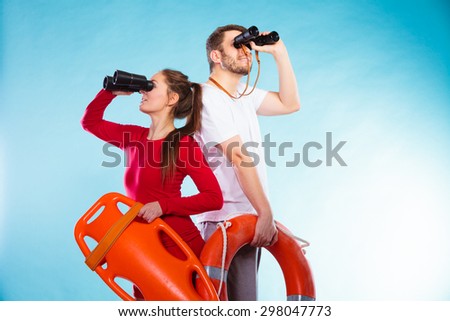 Accident prevention and water rescue. Young man and woman lifeguards on duty looking through binoculars keeping buoy lifesaver equipment on blue