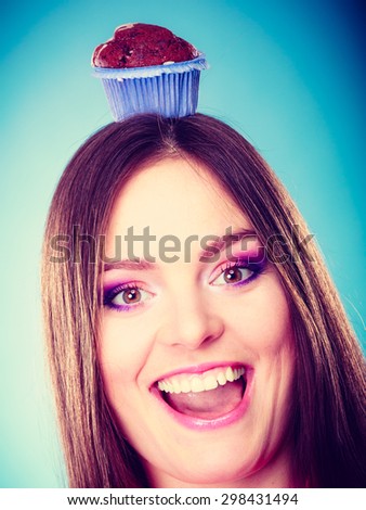 Sweet food sugar make us happy. Smiling crazy woman holds cake chocolate muffin on head blue background
