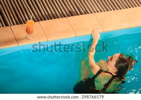 Woman in black dress relaxing at swimming pool edge poolside. Young girl with tropical drink cocktail resting. Leisure.