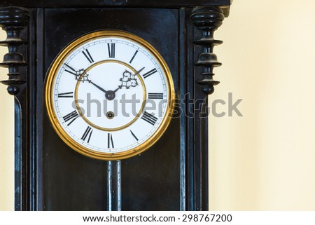 Closeup old big wooden pendulum clock hanging on wall