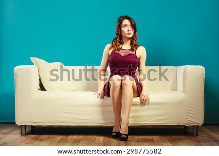 Fashion young woman in full length. Girl in fashionable dress high heels sitting on couch vivid color blue background