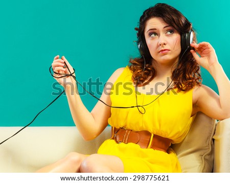 Young people leisure relax concept. Teen cute girl yellow dress in headphones listening music mp3, sitting on couch relaxing green blue background