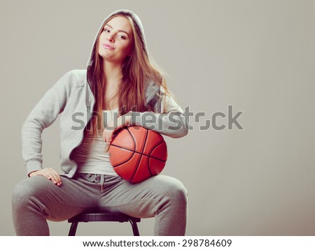 Sporty teenager girl wearing hooded sweatshirt holding basketball sitting on chair. Teen sport.