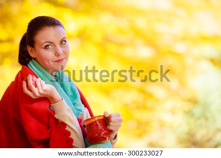 Happiness carefree and nature. Young woman relaxing in the autumn park enjoying hot drink coffee or tea, holding red mug with warm beverage. Yellow leaves background
