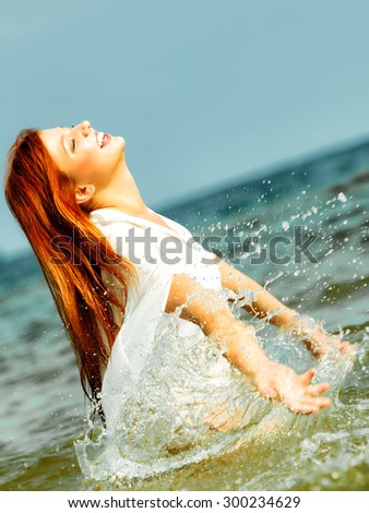 Vacation. Girl splashing water on the coast. Young woman having fun relaxing on the sea. Summertime.