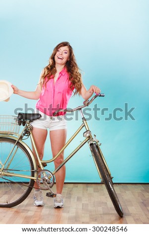 Happy joyful young woman with bike bicycle. Fashionable girl in pink shirt and shorts holding hat. Summer fashion and recreation. Studio shot.