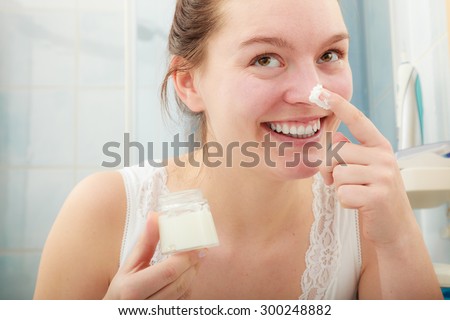 Happy young woman applying cleansing moisturizing skin cream on face. Girl taking care of dry complexion layering moisturizer. Skincare.