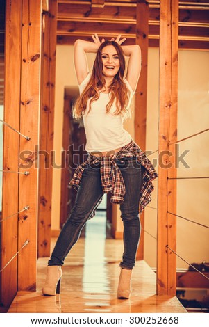 Happy cute pretty gorgeous woman at home showing bunny ears gesture. Attractive young girl with long hair wearing white shirt, jeans trousers and high heels. Instagram filter.