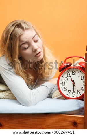 Unhappy woman waking up in bed with alarm clock. Young girl in the morning.