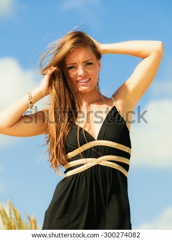 Vacation day on beach. Smiling happy standing woman black dress on sand.