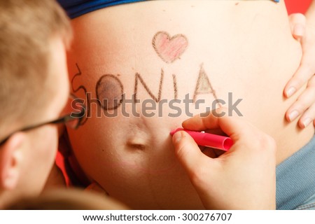 Pregnancy, parenthood and happiness concept. Family expecting new baby, having fun, man painting name of unborn baby girl writing on belly of pregnant woman