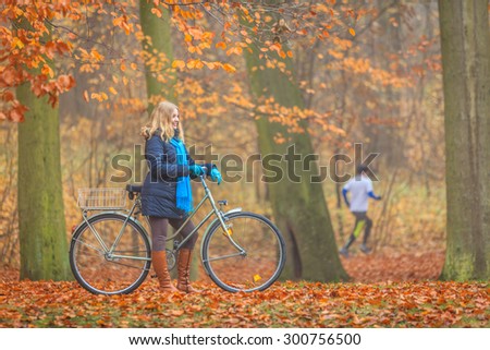 Happy active woman riding bike bicycle in fall autumn park. Glad young girl in jacket and scarf relaxing. Healthy lifestyle and recreation leisure activity.